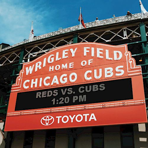 The image shows the marquee of Wrigley Field, home of the Chicago Cubs, displaying information for a game between the Reds and Cubs at 1:20 PM.