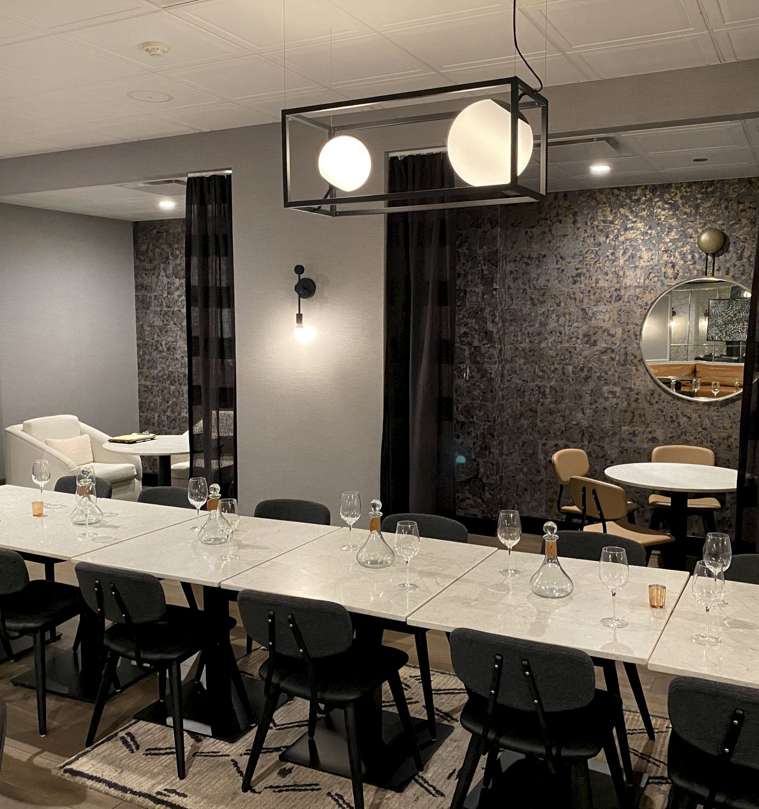 A stylish, modern dining area with a long table set for a meal, wine glasses, black chairs, and contemporary lighting and decor.