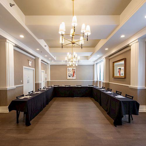 A well-lit conference room with a U-shaped table arrangement, black tablecloths, modern chandelier, and framed artwork on the walls.