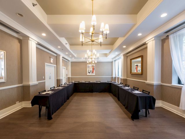 A well-lit conference room with a U-shaped table arrangement, black tablecloths, modern chandelier, and framed artwork on the walls.