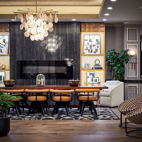 A modern, elegantly furnished dining room features a dark accent wall, framed artwork, a wooden table with chairs, plants, and a unique circular chandelier.