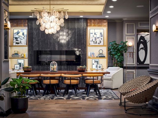 A modern, elegantly furnished dining room features a dark accent wall, framed artwork, a wooden table with chairs, plants, and a unique circular chandelier.