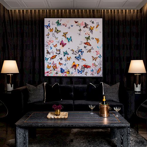 A stylish, dark-toned living room with a black sofa, two lamps, a coffee table, and a colorful butterfly artwork on the wall, creating a sophisticated ambiance.