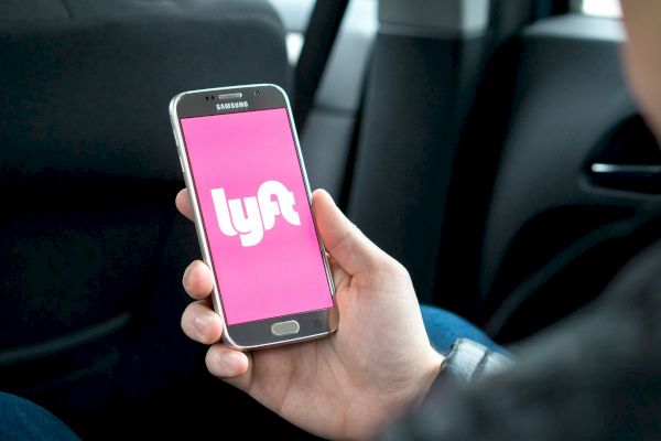 A person is holding a smartphone displaying the Lyft app while sitting in a car.