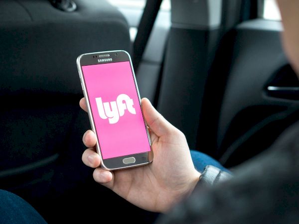 A person is holding a smartphone displaying the Lyft app while sitting in a car.