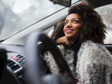 A person in a cozy sweater sits in a car, looking contently out the window on a rainy day, with a serene expression on their face.