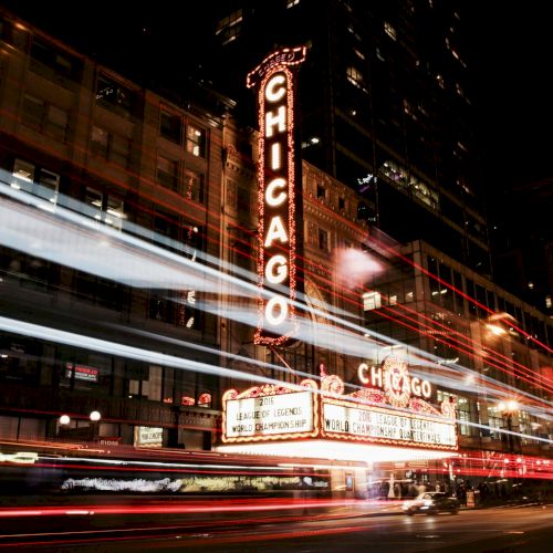 It's a nighttime scene featuring the iconic Chicago Theatre sign, with light trails from vehicles creating dynamic streaks across the image.