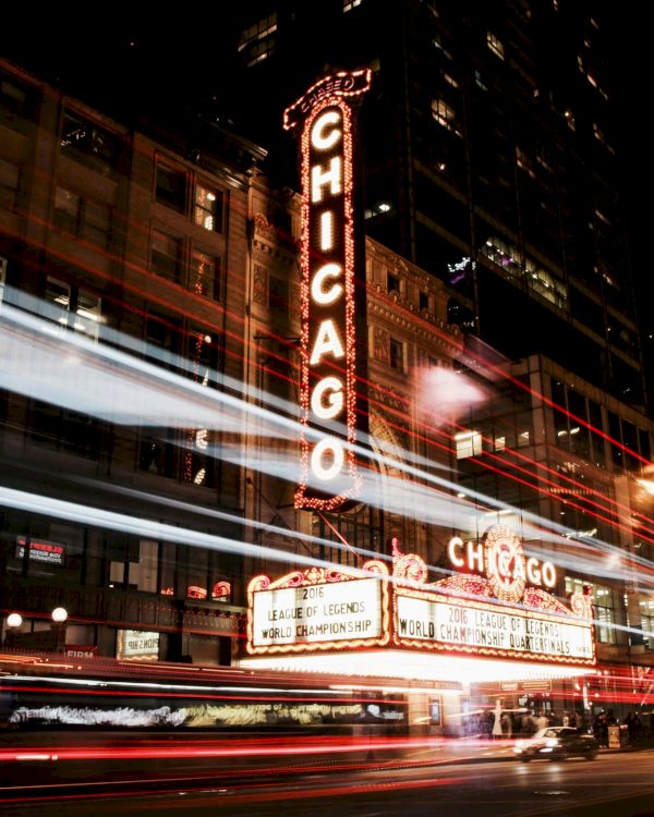 It's a nighttime scene featuring the iconic Chicago Theatre sign, with light trails from vehicles creating dynamic streaks across the image.