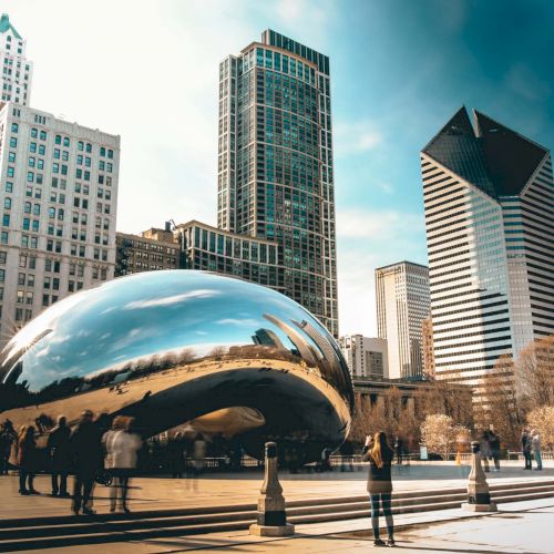 The image shows Chicago's Cloud Gate sculpture, known as "The Bean," with surrounding skyscrapers and people milling around.