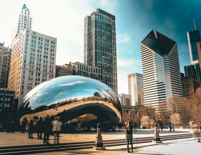 The image shows Chicago's Cloud Gate sculpture, known as "The Bean," with surrounding skyscrapers and people milling around.