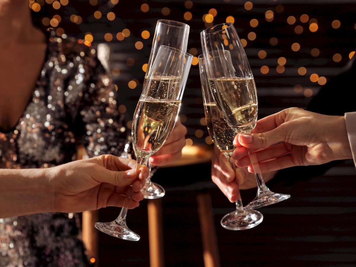 People toasting with champagne flutes at a celebration, with festive lights in the background.