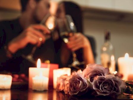 A romantic setting with two people toasting wine surrounded by candles and roses, creating an intimate and cozy atmosphere.