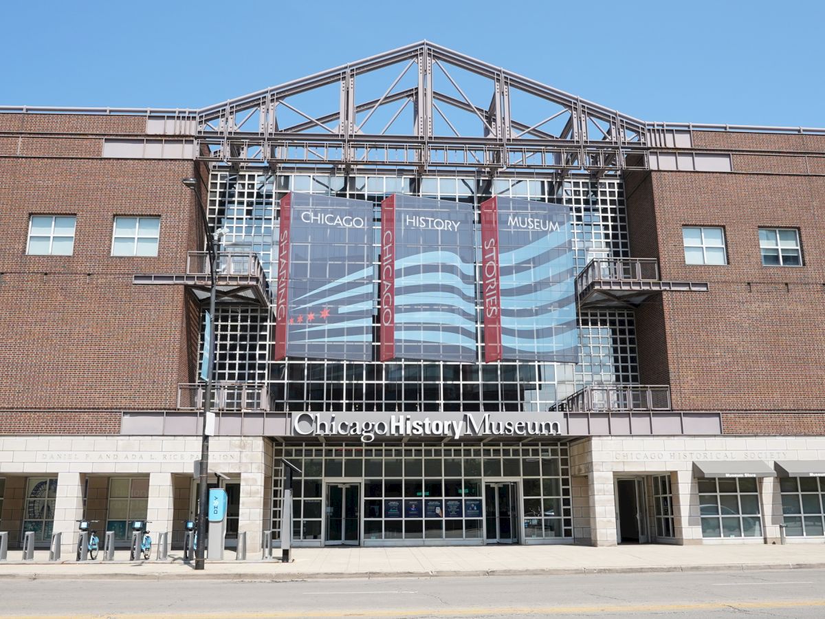The image shows the entrance of the Chicago History Museum, with banners and signage on a brick and glass building.