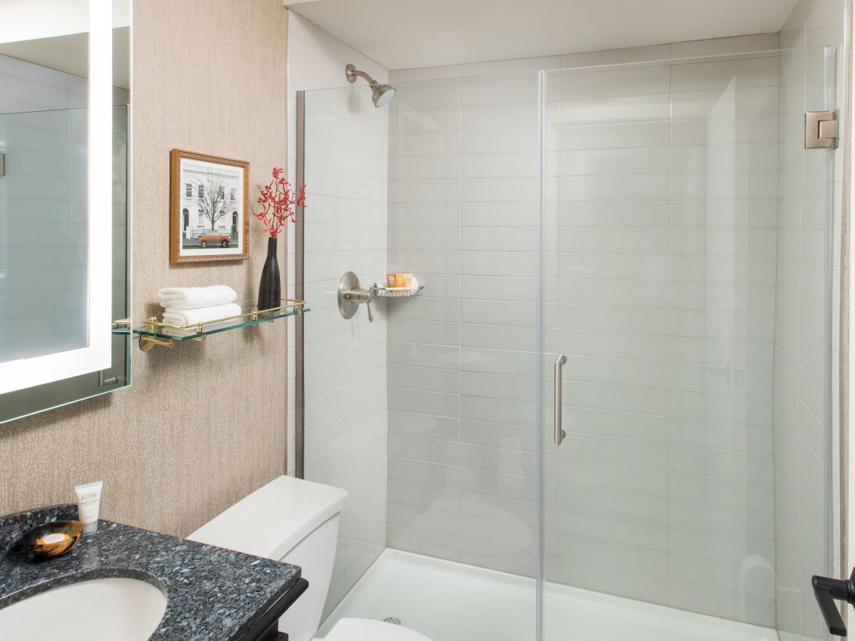 A compact modern bathroom with a glass shower enclosure, white fixtures, a dark granite countertop, and soft beige walls, neatly arranged.