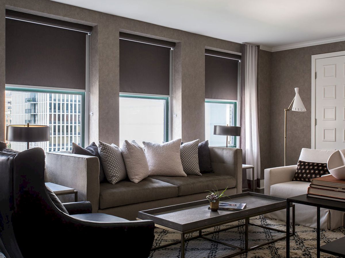 A modern living room with a gray sofa, black armchairs, coffee table, multiple throw pillows, floor lamps, and large windows with blinds, cozy and stylish.