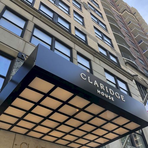 The photo shows a building entrance with a canopy and a sign reading &ldquo;___" (likely a hotel or office).