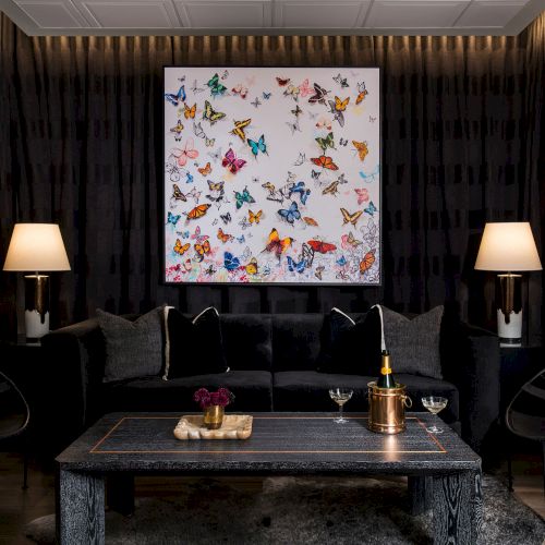 A dark living room with a framed floral artwork above a couch, two table lamps, and a coffee table in front.