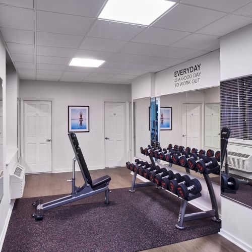 A small medical or clinical exam room with a bed, overhead light, cabinets, and blue chairs; clean and clinical.