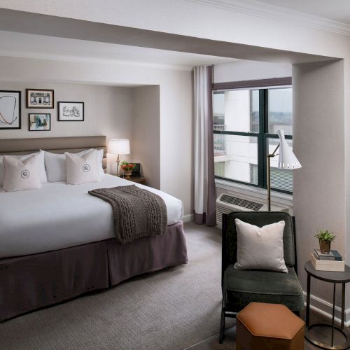 A stylish hotel bedroom with a large bed, dark wood furniture, a seating area, and a soft, neutral color palette.