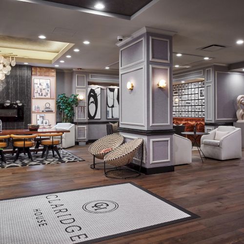 Cozy modern cafe or coworking space with a long wooden table, plants, hanging lights, and a kitchenette area in the background, inviting and bright.