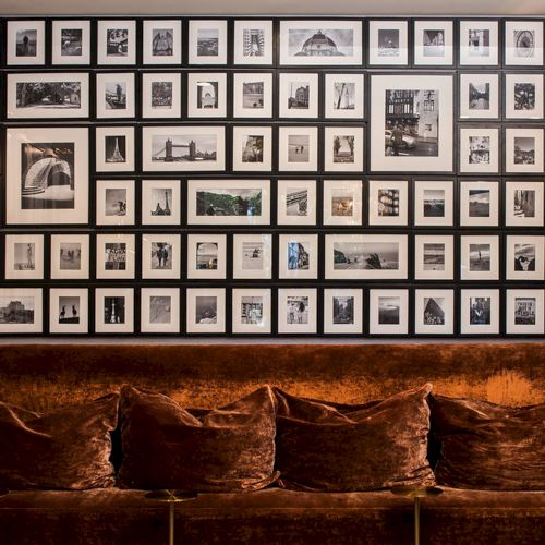A living room with a wall of framed photos above a wooden sideboard; warm lighting and a vintage, cozy feel.
