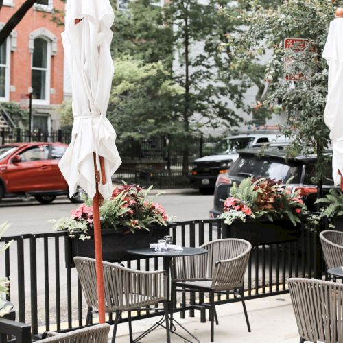 A quaint European-style courtyard with outdoor tables, chairs, potted plants, and a fountain between pastel buildings, charming and sunny.