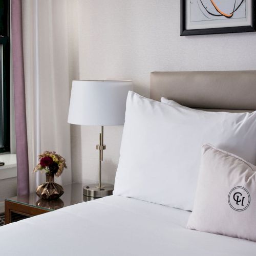 A bright, cozy bedroom with white bedding, a large window, and framed art above the bed, creating a calm, airy retreat.